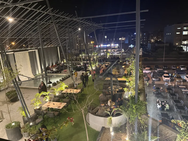The Mellow Terrace rooftop at night, tables between planters above Bahria Town